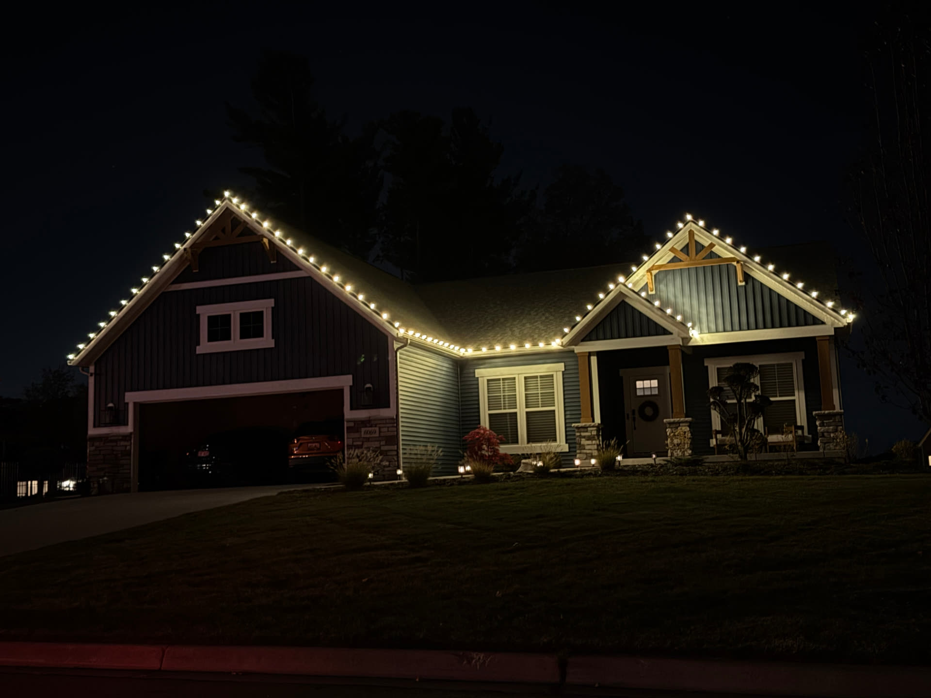 Craftsman ranch home with warm white lights tracing the garage and entry gables