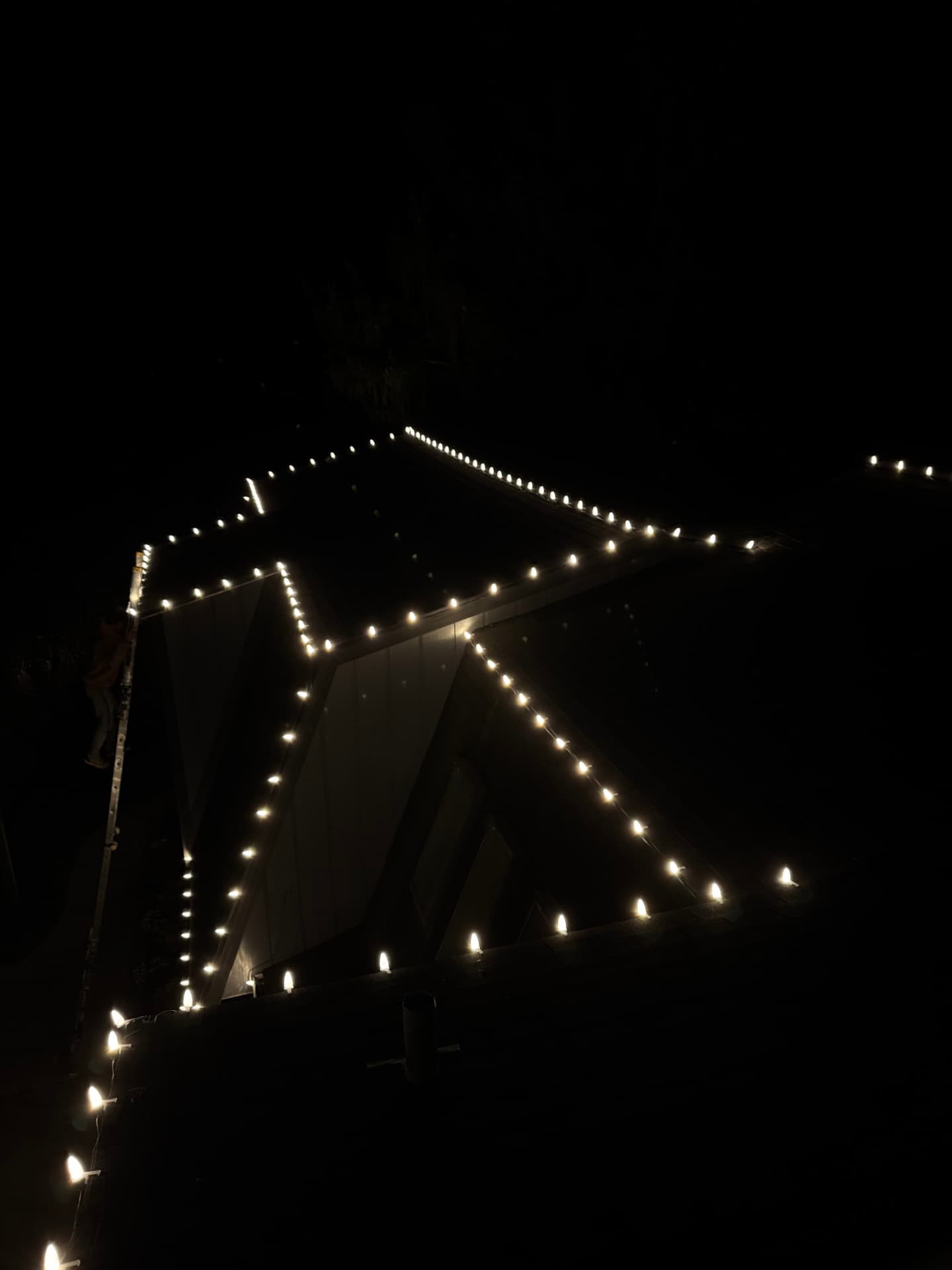 View from a ladder looking down a lit rooftop, bulbs spaced evenly along each edge